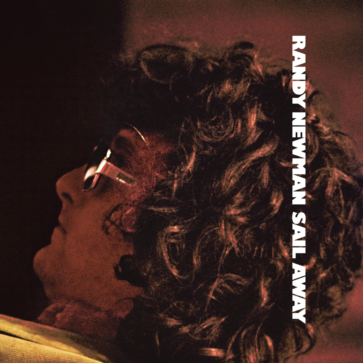 Album cover art for Randy Newman's 'Sail Away', featuring a close-up profile of a person with curly hair wearing sunglasses, tinted in warm red and orange tones against a dark background, with the text 'RANDY NEWMAN SAIL AWAY' printed vertically on the right.