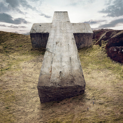 Large concrete cross structure in a grassy field with a cloudy sky.