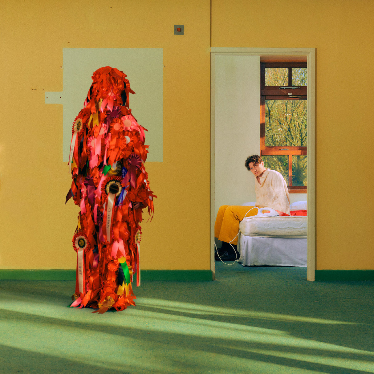 Person in a colorful, leaf-like costume standing in a room with a bed and window.