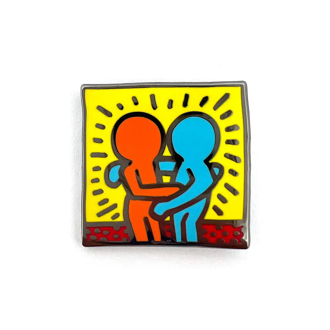 A pin with a colorful design featuring two stick figures hugging against a yellow background, with a red border.