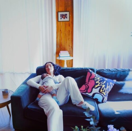 A person sitting on a couch holding a baby, with a pillow behind them featuring a colorful, abstract design.