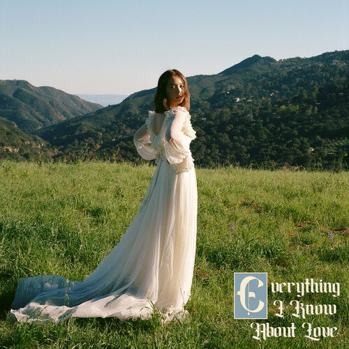 A person in a white dress standing in a field with mountains in the background, holding a album cover with the text 'Everything I Know About Love'.