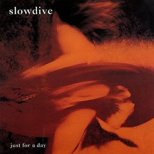 This image features the album cover for "Just For A Day" by Slowdive, a classic English rock band. The artwork is a striking, ethereal photograph of a figure, likely a female, in a sensual pose with a blurred, indistinct background.