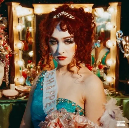 An album cover featuring a person with red hair and makeup, wearing a blue dress with sequins, standing in front of a mirror with reflections of lights and costumes.