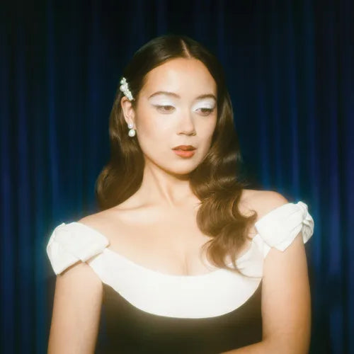 An image of a woman with light makeup, wearing a white off-shoulder top, with a blue backdrop. This is presumably the artist Laufey for the album 'Bewitched: The Goddess Edition 2LP'.