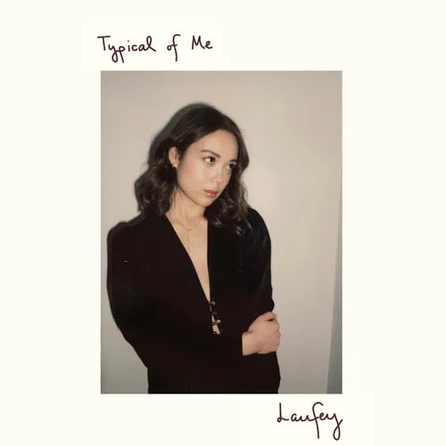 An album cover featuring a photograph of a person with their arms crossed, wearing a black top, with the title ' Typical of Me' and the artist's name 'Laufey' printed at the top and bottom.