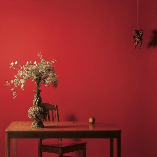 A red album cover featuring a vase with flowers on a table against a red background, with a small figure hanging on the wall in the background.
