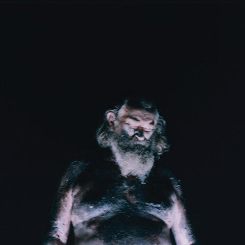 Person with long hair and beard wearing a dark outfit against a black background