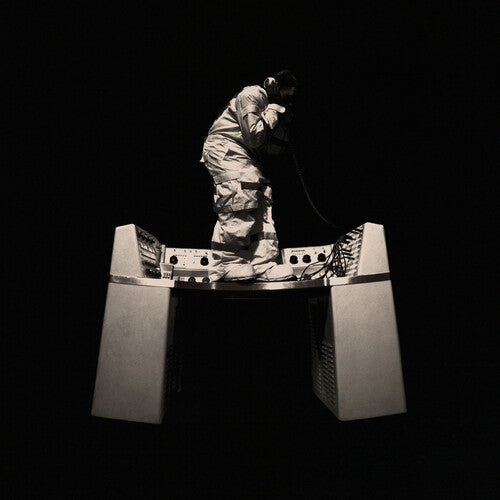 Person in a protective suit standing on a large metallic object against a black background