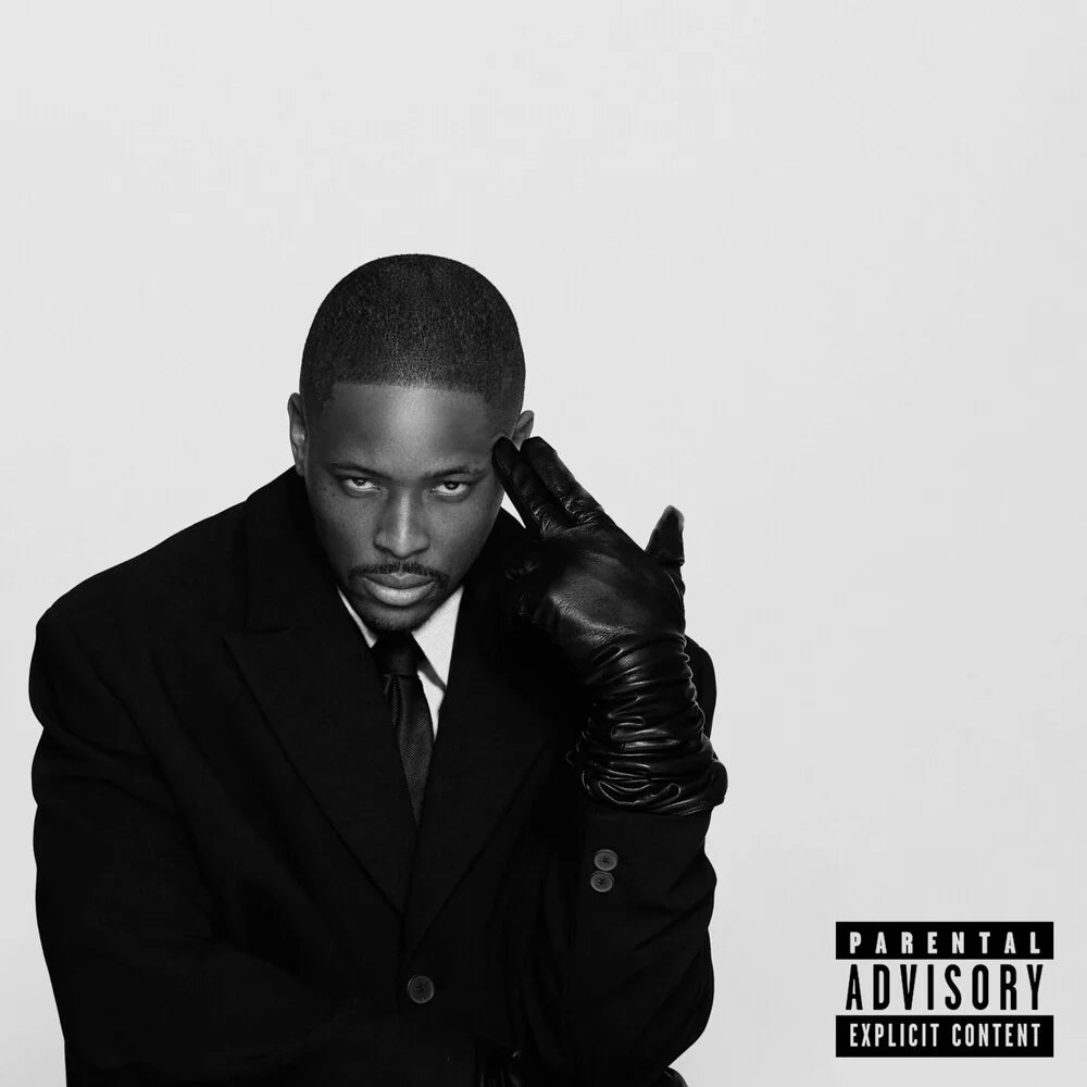 A black and white portrait of a man in a dark suit and tie, wearing a black leather glove on one hand while resting it against his face. The image has a black 'Parental Advisory Explicit Content' label in the bottom right corner on a light gray background.