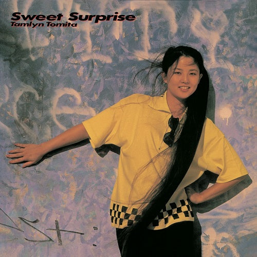 Album cover with a person in a yellow shirt and black pants against a textured background, featuring the text 'Sweet Surprise' and 'Tamlyn Tomita'.