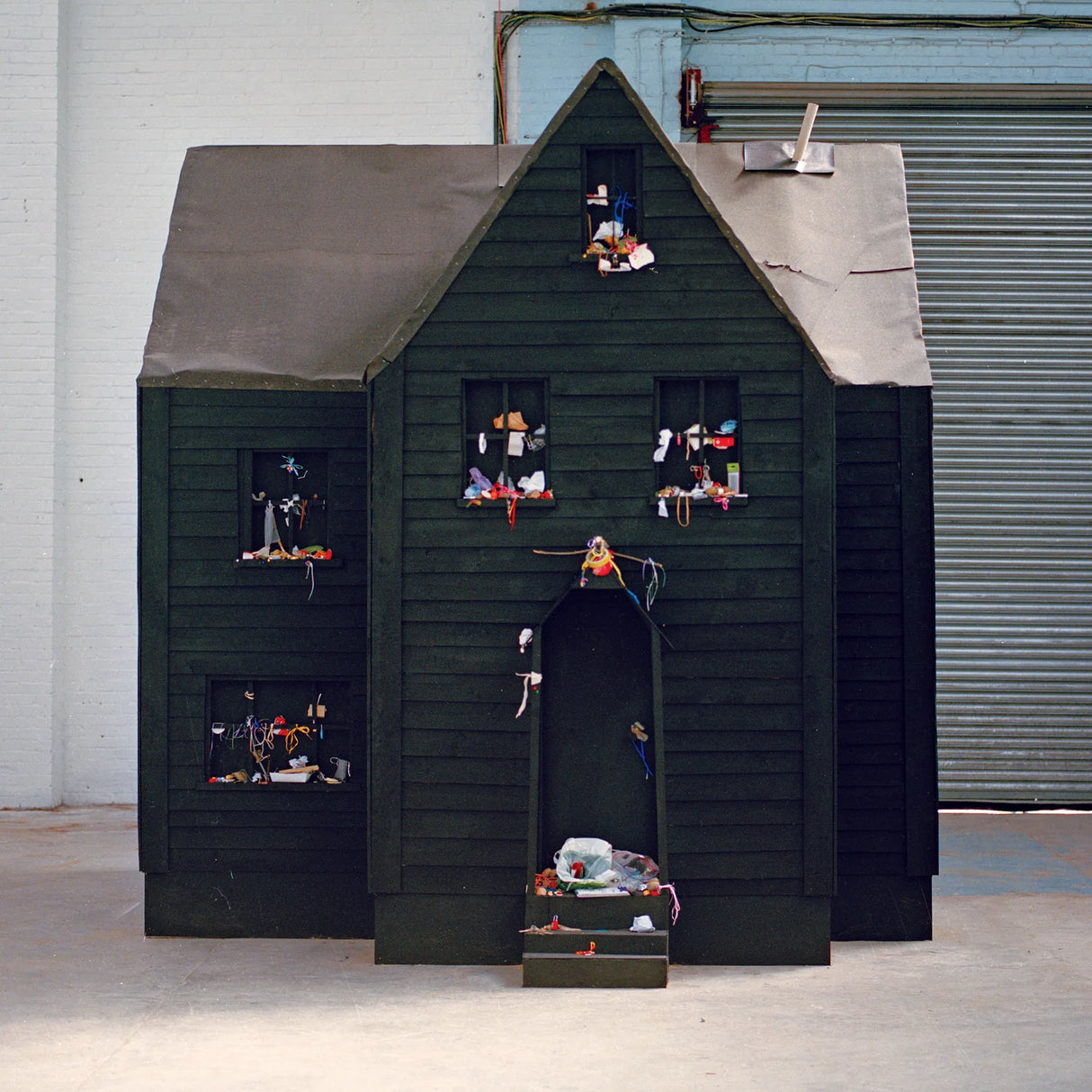 Dark wooden playhouse with small figures and objects on shelves against a plain background
