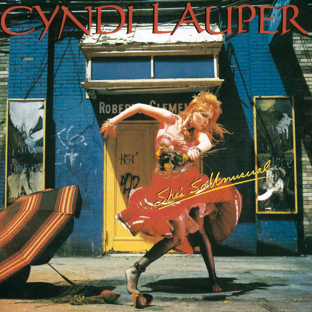 Album cover with a person in a red dress dancing in front of a blue wall with graffiti and text.