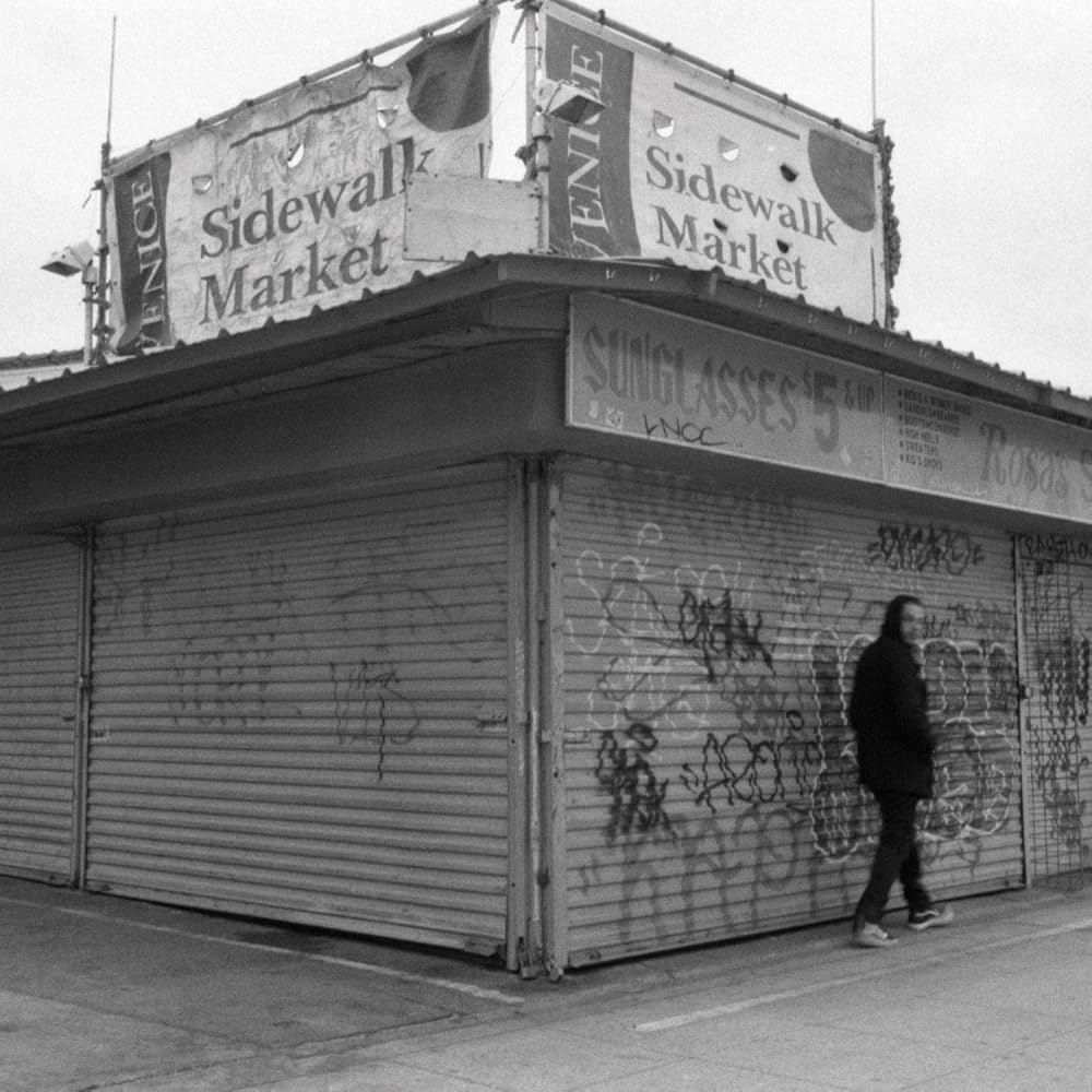 Person standing in front of a closed storefront with graffiti, labeled 'Sidewalk Market'.