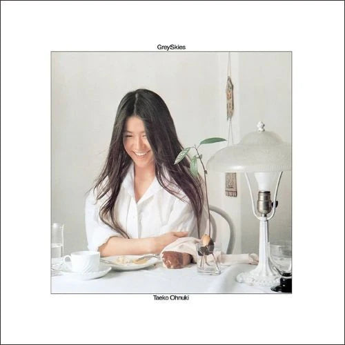 The image depicts the album cover for "Grey Skies" by Taeko Ohnuki. The cover features a photograph of Taeko Ohnuki, a woman with dark hair, smiling brightly.