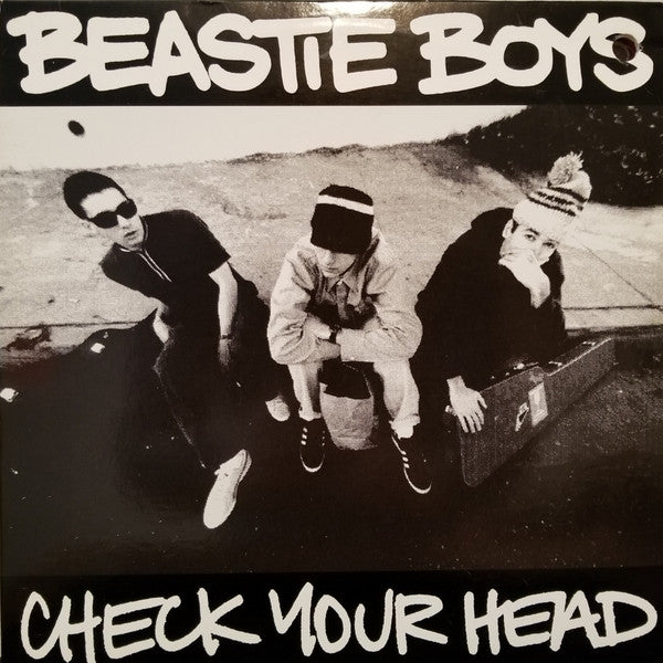 Album cover of 'Check Your Head' by Beastie Boys featuring three members sitting outdoors.