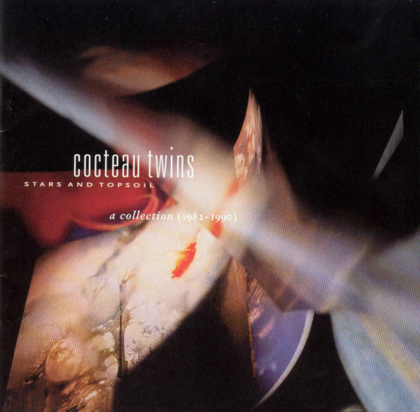 Album cover for Cocteau Twins' 'Stars And Topsoil A Collection (1982-1990)'. The cover features an abstract, blurred image with red accents, typical of the band's artistic style.