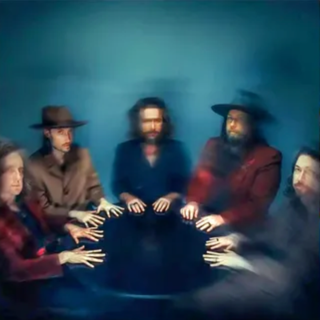 A group of five members from My Morning Jacket wearing various colored jackets and hats, seated in a circle with their hands palm-up in front of them against a blue background.