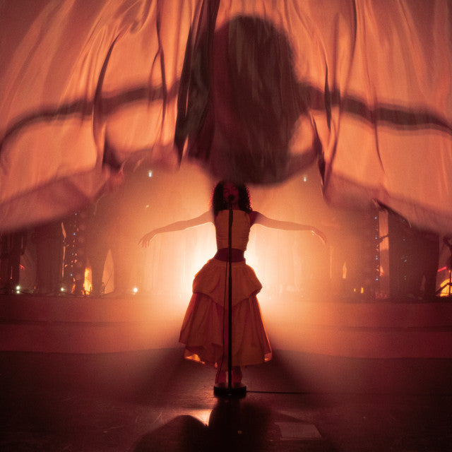Person in a white dress standing on a stage with a warm, orange glow