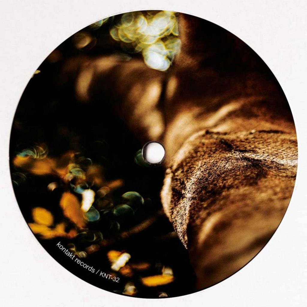 A circular vinyl record or CD cover featuring a close-up abstract photograph of a textured brown surface with warm golden highlights and dark shadows. Small white text in the lower-left reads 'kontakt records / kni-32'.