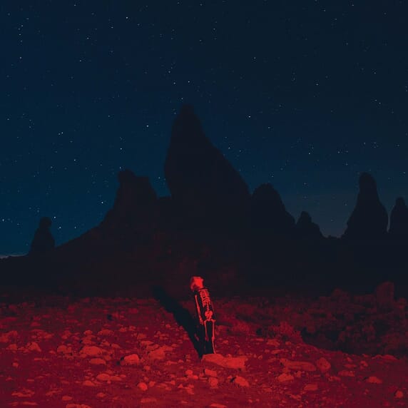 A person standing in a red-lit landscape with silhouetted rock formations in the background under a starry sky.