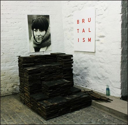 The image displays a vinyl record titled "IDLES - Brutalism LP," prominently featuring a photo of a woman on the cover. The cover is minimalistic, with the band's name and the album title in bold red and white text.