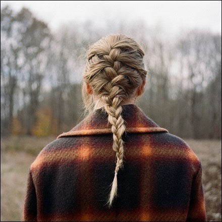 A person with a braid hairstyle wearing a plaid jacket, viewed from the back against an outdoor backdrop.