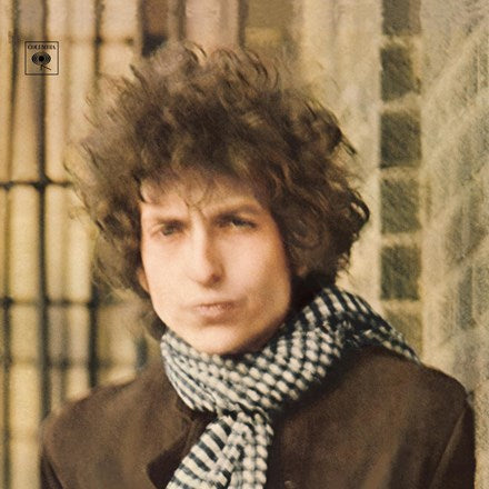 The cover image shows Bob Dylan with curly hair and a scarf around his neck, looking directly at the camera. The background is blurred, making it difficult to identify the setting.