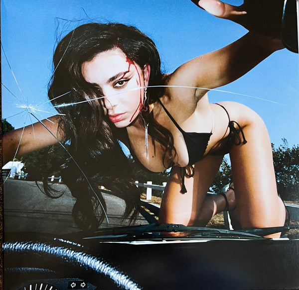 This image features the album cover of "Charli XCX - Crash LP." It displays a vivid and dramatic photograph of the artist, Charli XCX, with a striking pose against a bright blue sky backdrop.