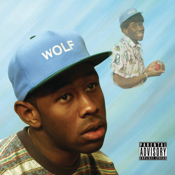 The image features the cover of the CD titled "Wolf" by Tyler The Creator. The cover artwork displays a portrait of Tyler in a casual, relaxed pose, wearing a blue cap with the word "WOLF" emblazoned on the front.