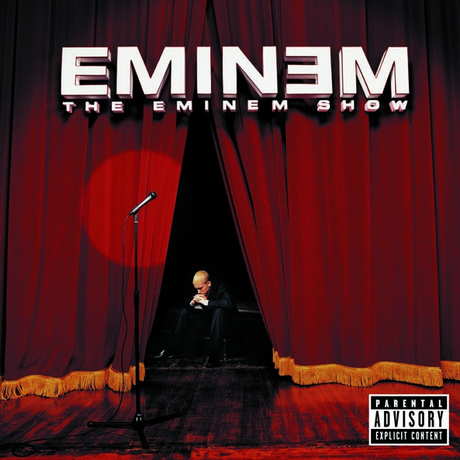 This image features the album cover for "The Eminem Show 2LP," showcasing a powerful and evocative design. The cover art displays a intense and solitary figure, Eminem, standing on a stage with a microphone, silhouetted against a vibrant red backdrop that resembles a setting sun through a curtain.