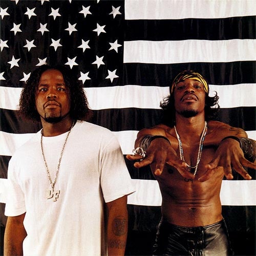 Two members of the OutKast hip hop group posing against a background with an American flag.