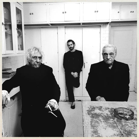 Three people in a kitchen setting, with white cabinets and a tiled wall.