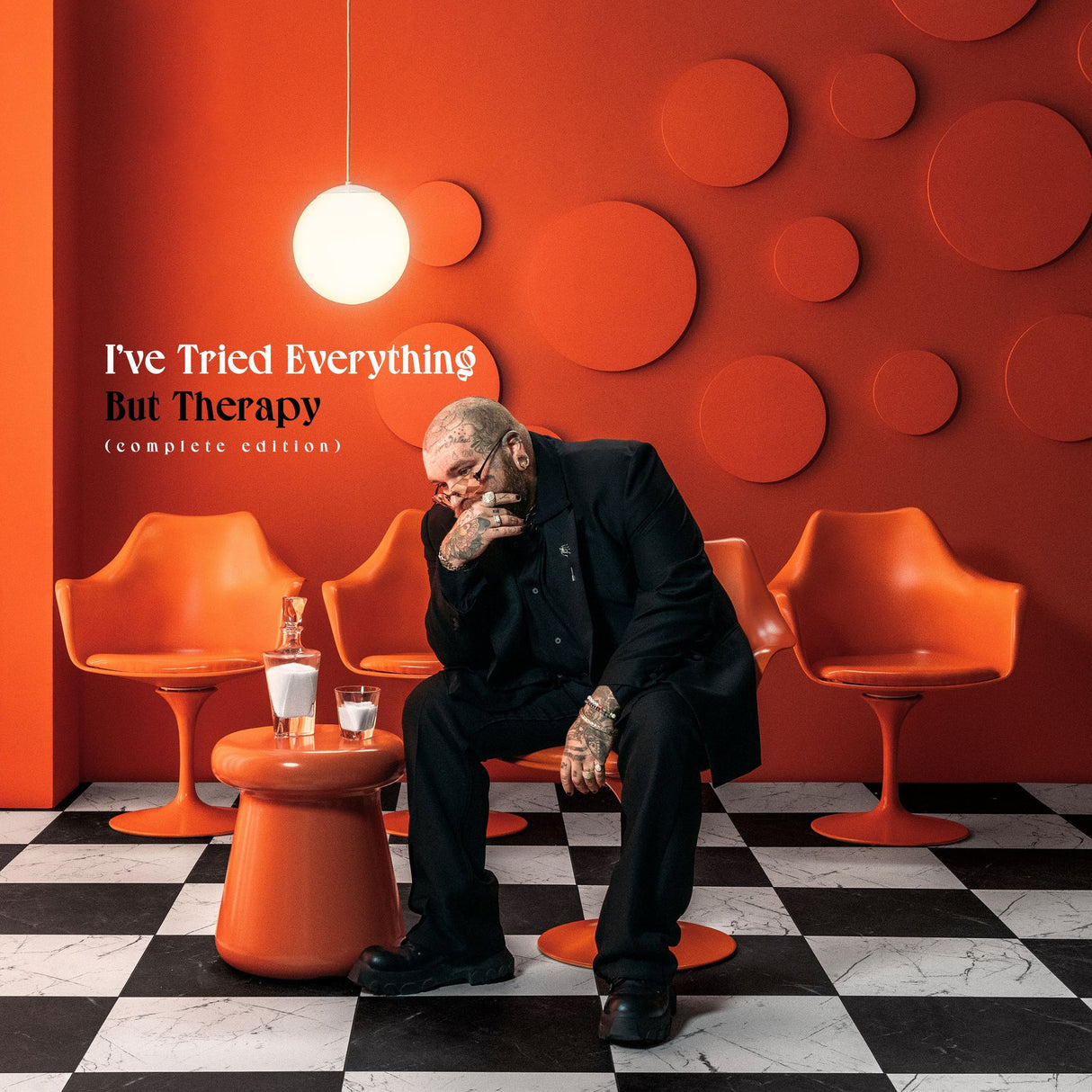 Person sitting in a modern room with orange chairs and a red wall, album cover for 'I've Tried Everything But Therapy'.
