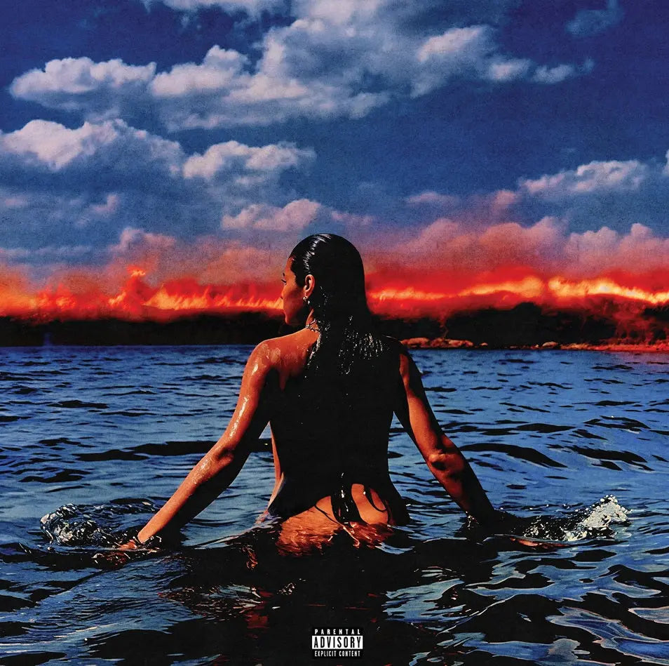 Person sitting in water with a dramatic sky and sunset in the background