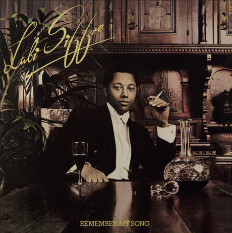 Album cover with a person sitting at a table with a glass and decanter, surrounded by decorative items.