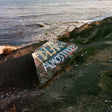 Graffiti-covered stone on a rocky shore with water in the background
