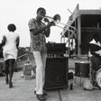 Man playing trombone outdoors with a band and audience in the background