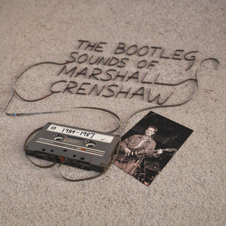 Cassette tape and photo with 'The Bootleg Sounds of Marshall Crenshaw 1984-1987' text on a textured surface.