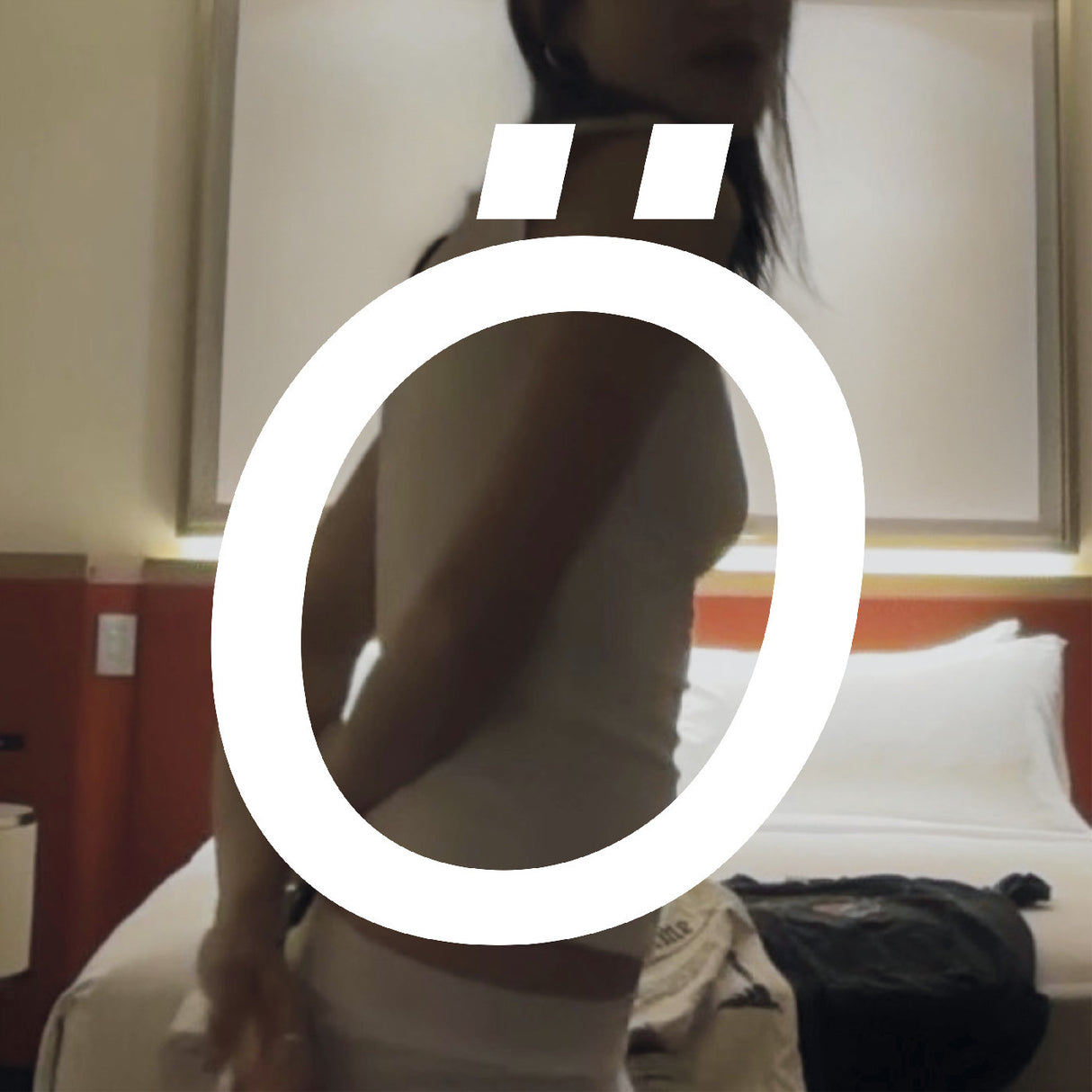 Person sitting on a bed with a blurred area over their face in a hotel room.