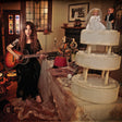 Person playing guitar in a room with a wedding cake and dolls.