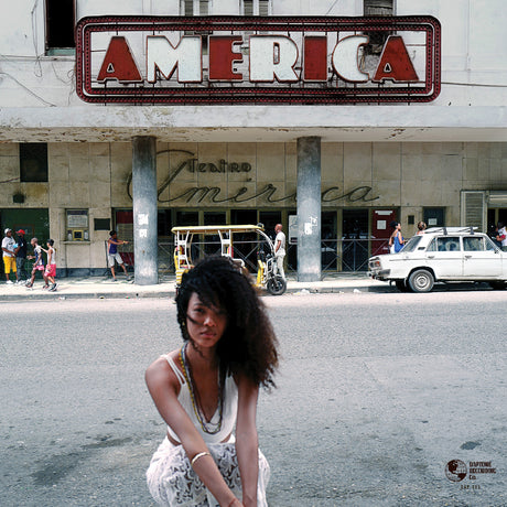 Woman squatting on a street in front of a building with 'America' sign