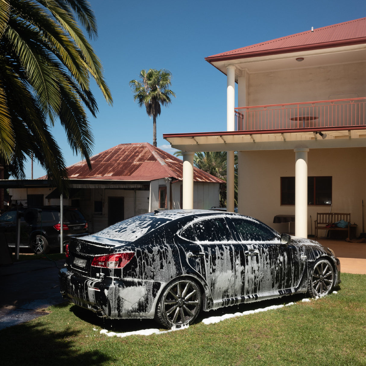 Car covered in soap suds parked in front of a house with palm trees.