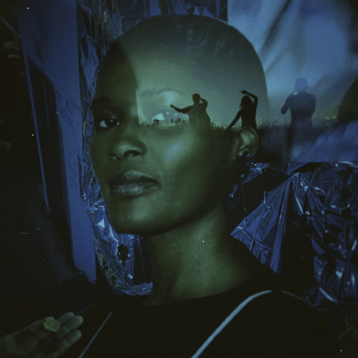 A dark, artistic portrait of a person with a shaved head, overlaid with silhouettes of figures and reflective metallic material, in blue-green and black tones.
