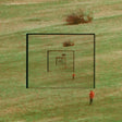 A square grassy field with concentric black target-like frames and a small person in an orange top standing near the bottom right, photographed from above.
