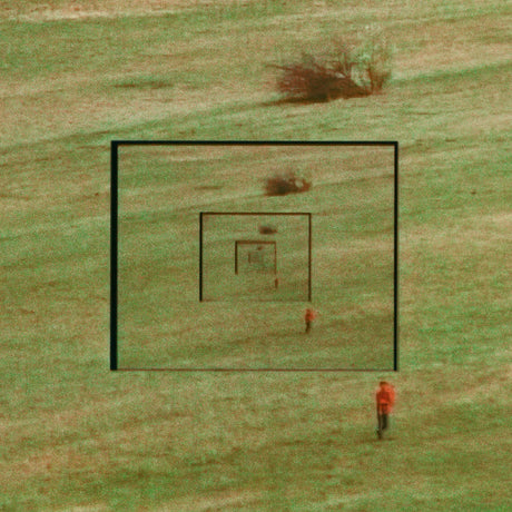 A square grassy field with concentric black target-like frames and a small person in an orange top standing near the bottom right, photographed from above.