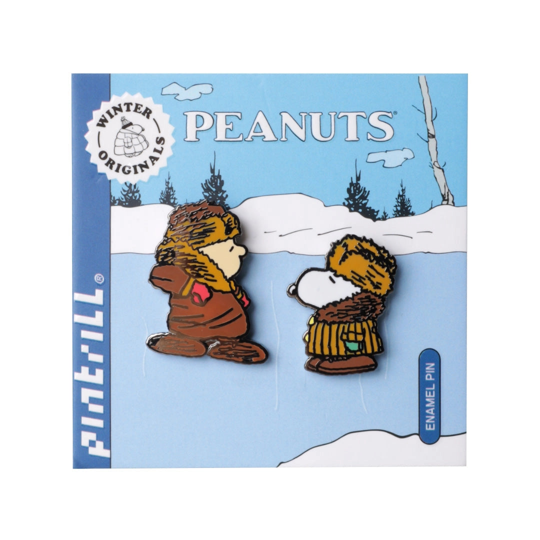 A pair of Peanuts enamel pins featuring Snoopy and Woodstock in winter clothing, mounted on a blue and white retail backing card. The backing card displays the 'Pintill' brand name on the left side, 'Winter Originals' logo at the top left, and 'Peanuts' branding at the top center.