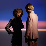 Two people standing against a colorful sky with a gradient of blue, purple, and pink.
