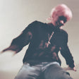 Person with pink hair sitting on a couch wearing a black sweatshirt with a graphic design.