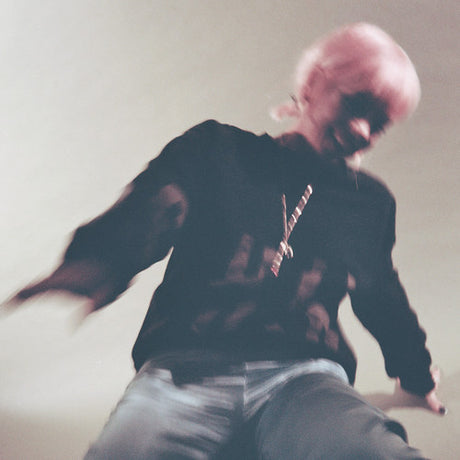 Person with pink hair sitting on a couch wearing a black sweatshirt with a graphic design.